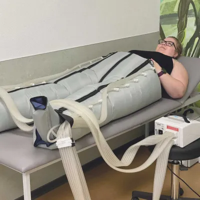 Patientin liegt mit Kompressionsmanschetten an Beinen bei AIK-Therapie.