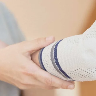 Hand hält Ellenbogen mit gestrickter Bandage in Weiß, Grau und Blau