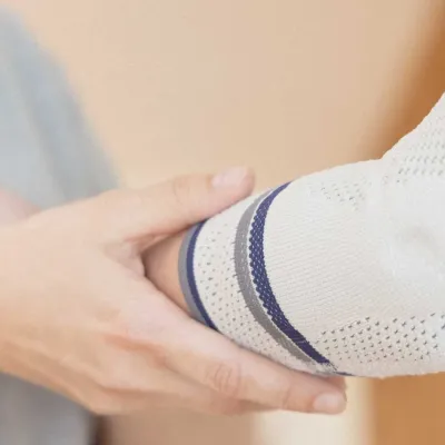 Hand hält Ellenbogen mit gestrickter Bandage in Weiß, Grau und Blau