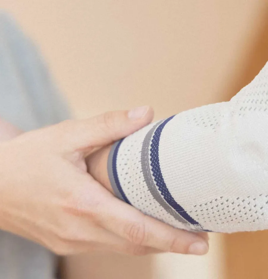 Hand hält Ellenbogen mit gestrickter Bandage in Weiß, Grau und Blau