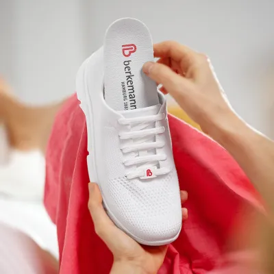 Hände heben herausnehmbare Einlegesohle aus weißem Berkemann-Schuh.