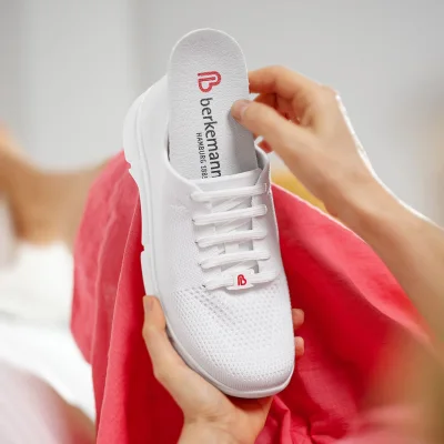 Hände heben herausnehmbare Einlegesohle aus weißem Berkemann-Schuh.