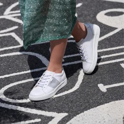 Weiße Sneaker mit grauen Details, dazu grüner Rock, auf Asphalt mit Linien.