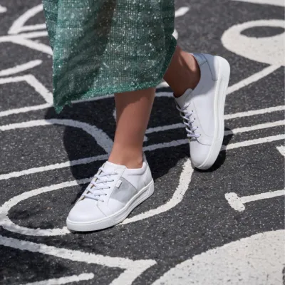 Weiße Sneaker mit grauen Details, dazu grüner Rock, auf Asphalt mit Linien.