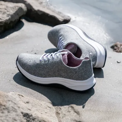 Graue Wollfilz-Sneaker mit weißer Sohle und pinkem Innenfutter am Strand