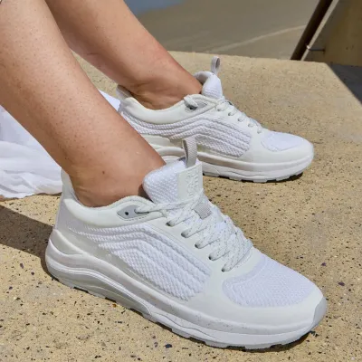 Weiße Sneaker mit gepolsterter Sohle, an den Füßen sitzend getragen.
