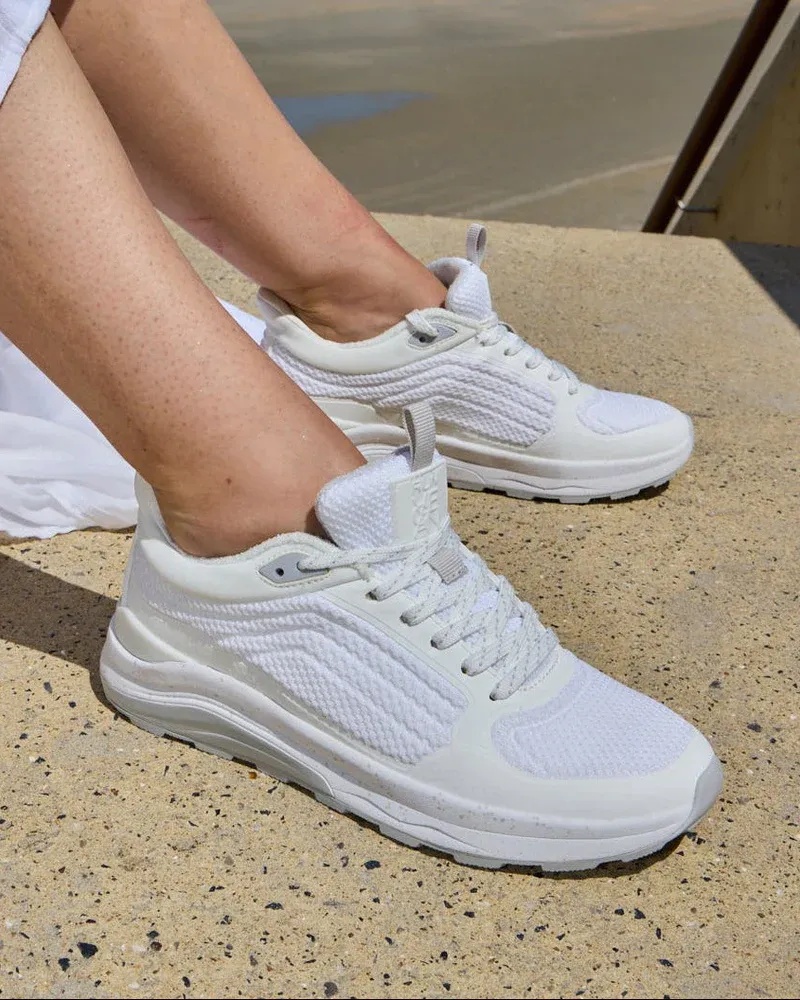 Weiße Sneaker mit gepolsterter Sohle, an den Füßen sitzend getragen.