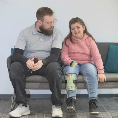 Mitarbeiter im Gespräch mit lächelndem Mädchen mit grüner Beinorthese