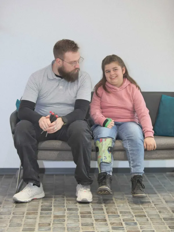 Mitarbeiter im Gespräch mit lächelndem Mädchen mit grüner Beinorthese