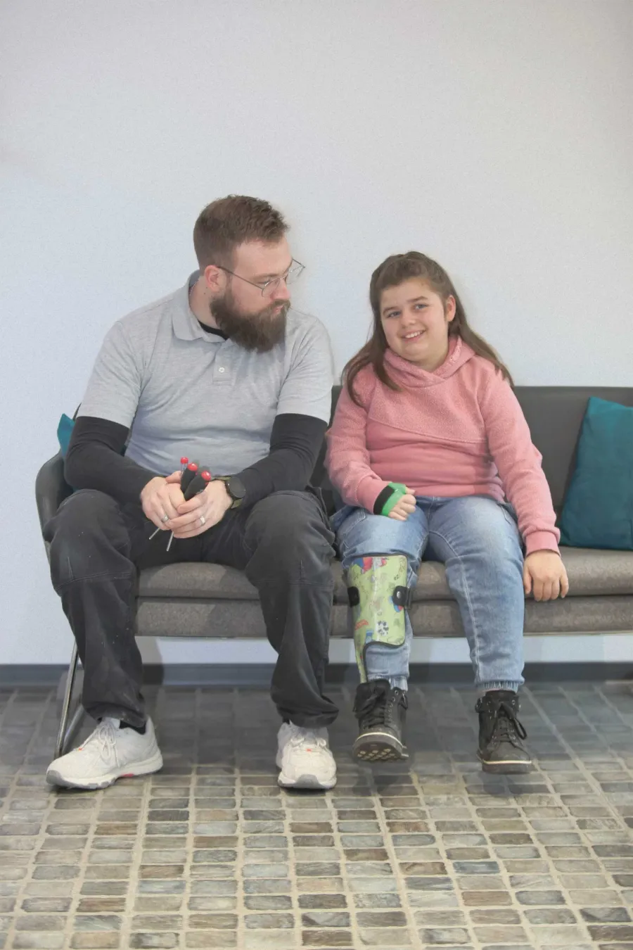 Mitarbeiter im Gespräch mit lächelndem Mädchen mit grüner Beinorthese