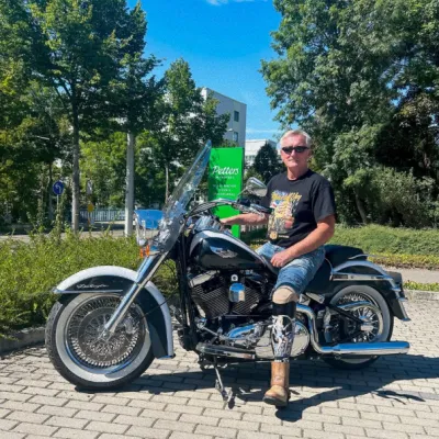 Mann mit Beinorthese sitzt auf Motorrad vor Petters-Filiale im Grünen.