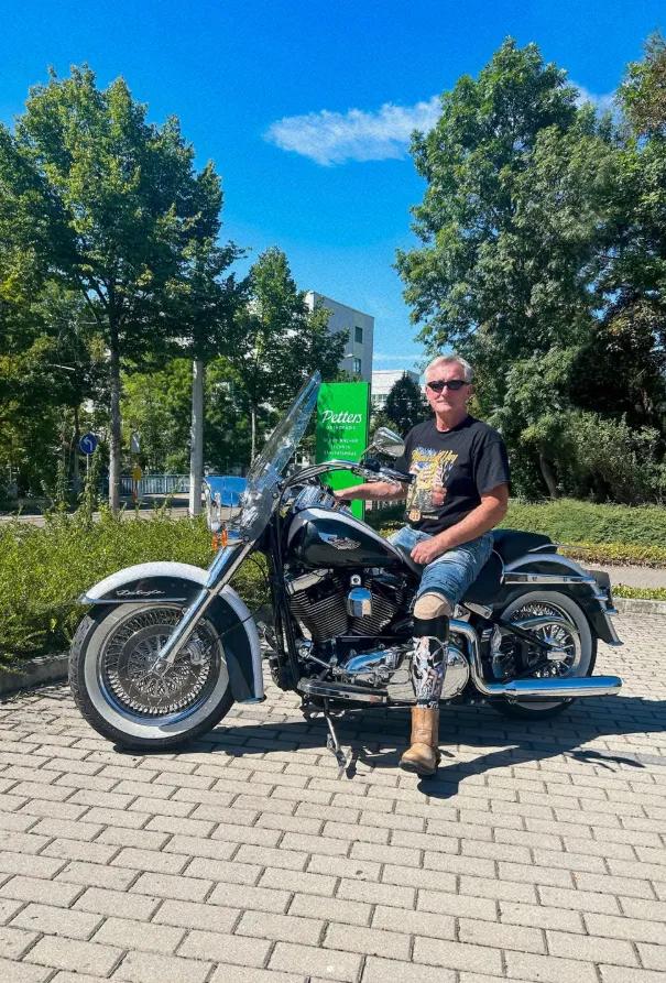 Mann mit Beinorthese sitzt auf Motorrad vor Petters-Filiale im Grünen.