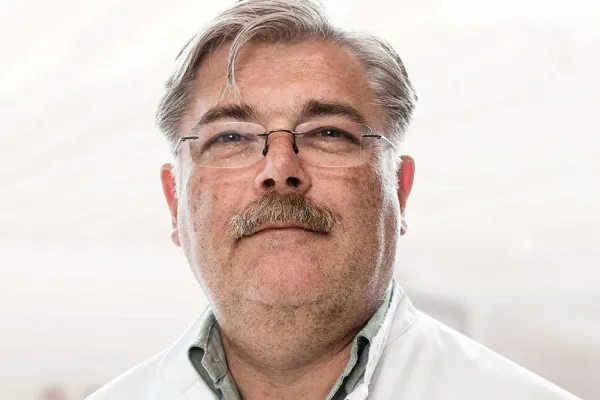Mitarbeiter mit Brille, Schnurrbart und weißem Kittel im Porträt