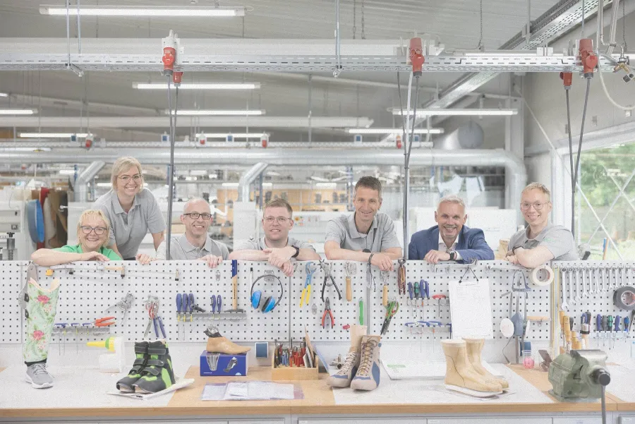 Team lehnt lächelnd an Werkbank mit Werkzeugen und orthopädischen Schuhen