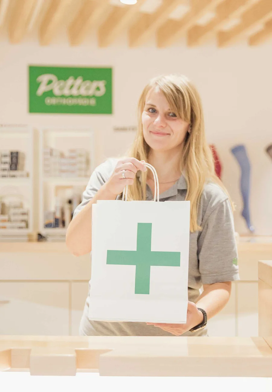 Mitarbeiterin überreicht Papiertüte mit grünem Kreuz im Petters-Ladengeschäft.
