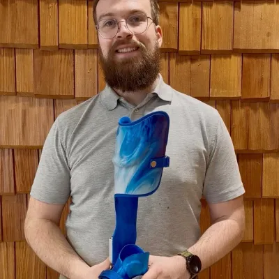 Mann hält blau marmorierte Beinorthese mit passendem Schuh in Händen.