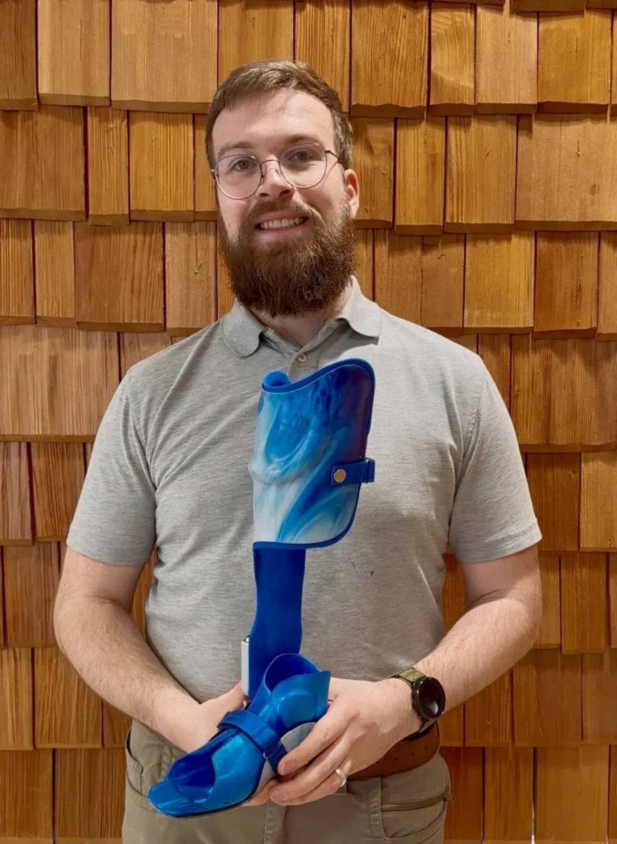 Mann hält blau marmorierte Beinorthese mit passendem Schuh in Händen.