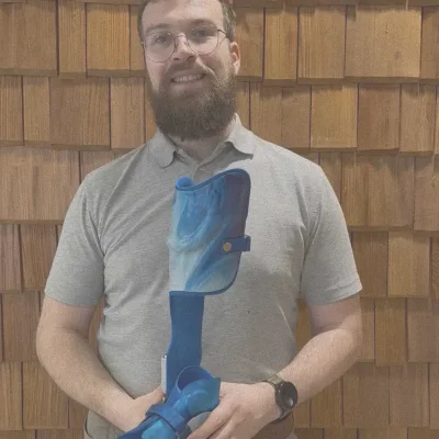 Mann hält blaue Unterschenkelorthese mit Fußteil in beiden Händen.