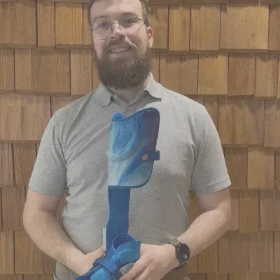 Mann hält blaue Unterschenkelorthese mit Fußteil in beiden Händen.