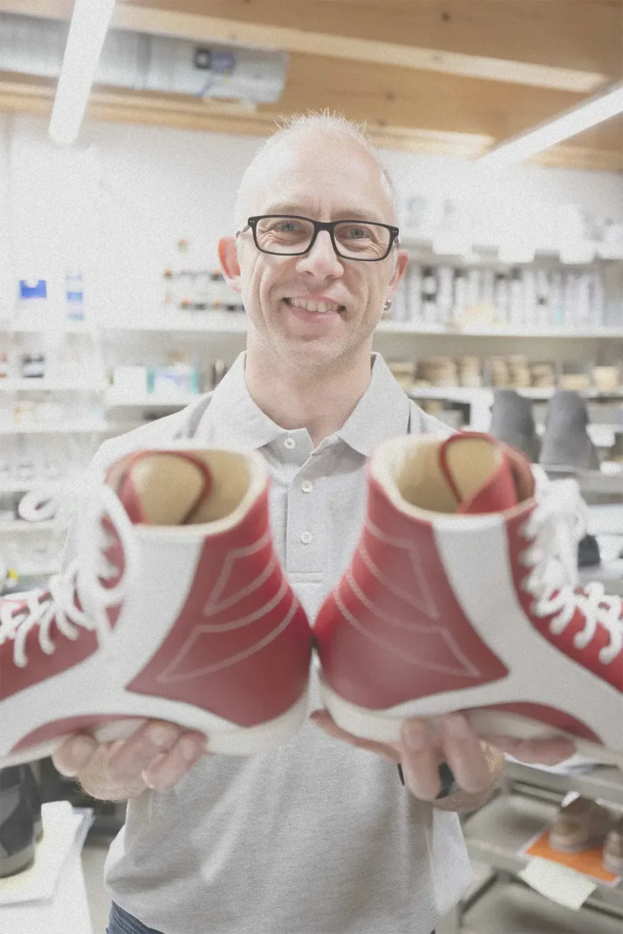 Mitarbeiter präsentiert ein Paar rot-weiße orthopädische Maßschuhe in der Werkstatt.