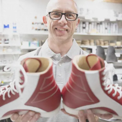 Mitarbeiter präsentiert lächelnd ein Paar rot-weißer orthopädischer Maßschuhe.
