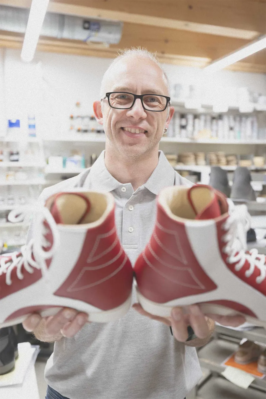 Mitarbeiter präsentiert lächelnd ein Paar rot-weißer orthopädischer Maßschuhe.