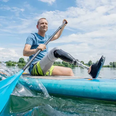 Mann mit Beinprothese paddelt sitzend auf einem Stand-Up-Paddle-Board