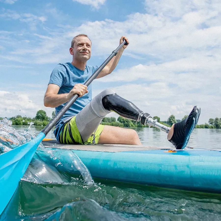 Mann mit Beinprothese paddelt sitzend auf einem Stand-Up-Paddle-Board