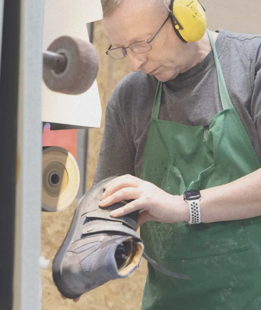 Orthopädieschuhmacher mit Gehörschutz prüft Schuh an Schleifmaschine