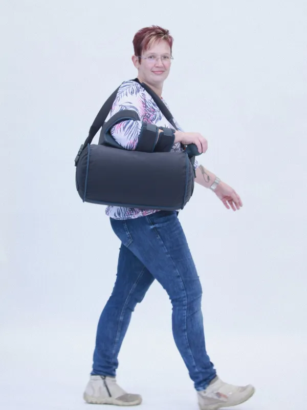 Frau mit Armorthese am Ellenbogen trägt gepolsterte Tasche gehend.