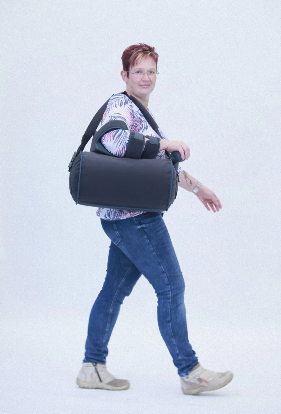 Frau mit Armorthese am Ellenbogen trägt gepolsterte Tasche gehend.