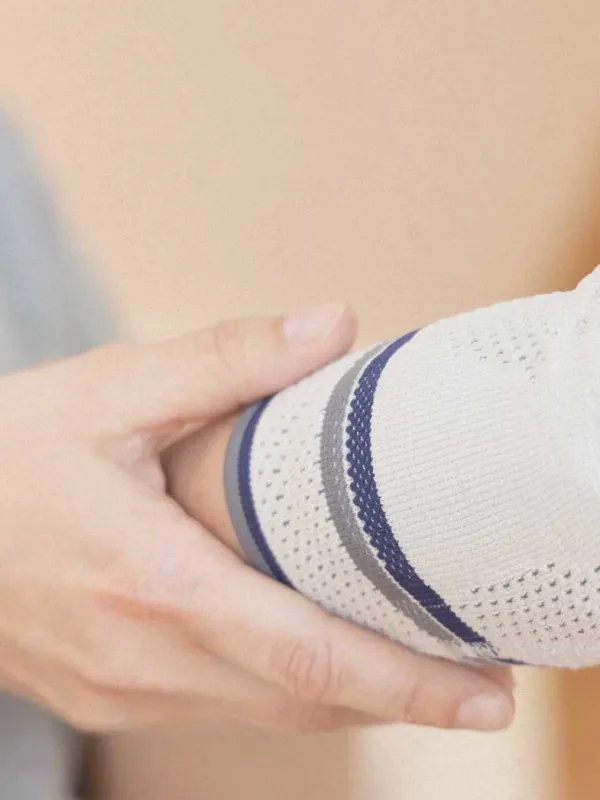 Hand hält Arm mit gestrickter Bandage in Weiß, Grau und Blau