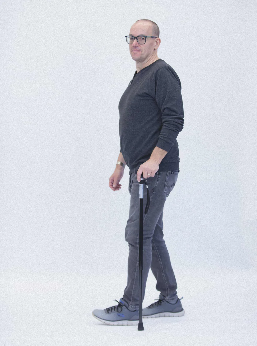 Mann mit Brille geht mit Gehstock, Seitenansicht vor hellem Hintergrund.