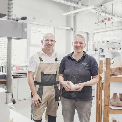 Zwei Mitarbeitende in Petters-Arbeitskleidung in der Werkstatt, sie hält einen Leisten.