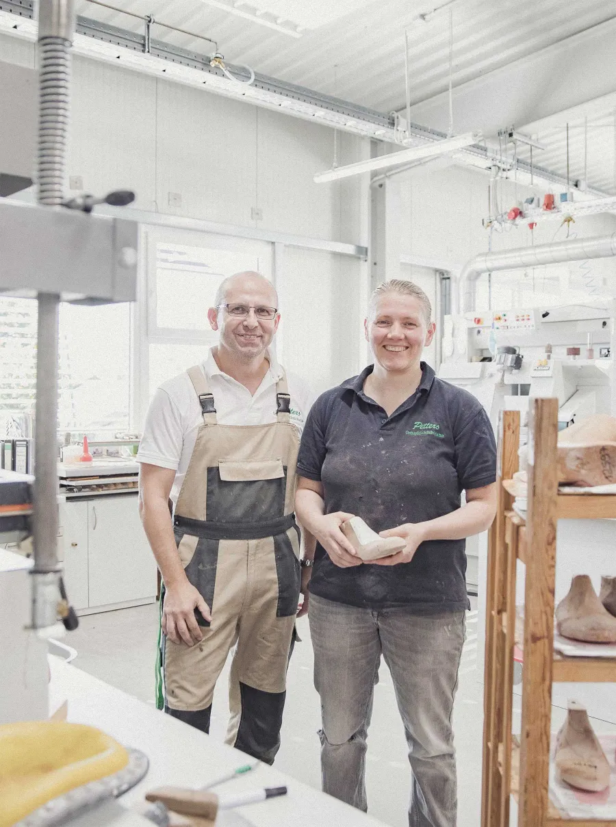 Zwei Mitarbeitende in Petters-Arbeitskleidung in der Werkstatt, sie hält einen Leisten.