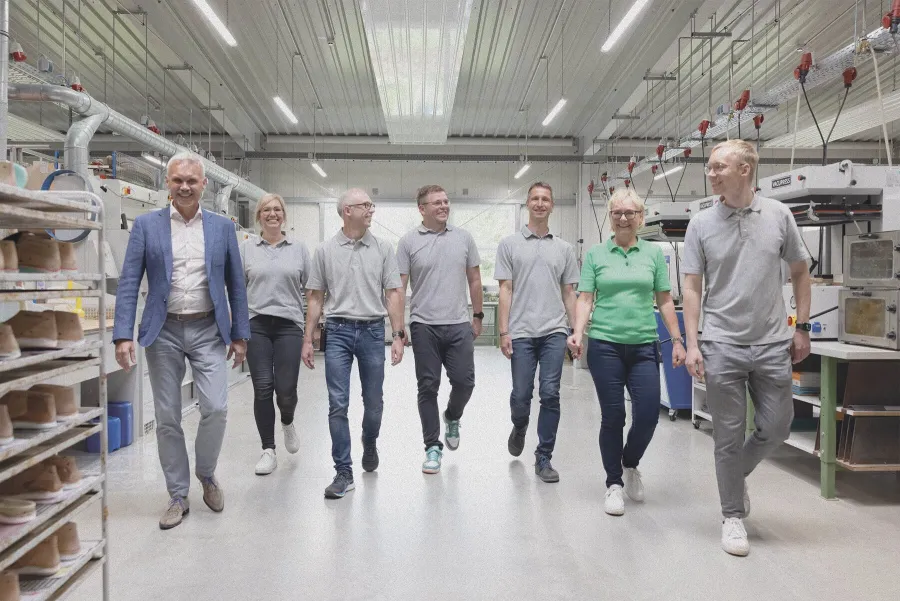 Team geht lächelnd durch Werkstatt mit Maschinen und Schuhleisten